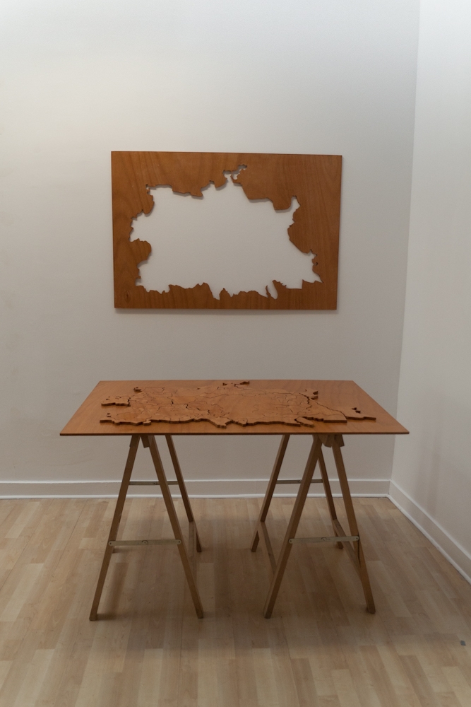 Personal Cartography, interactive wooden puzzle game. Black pencil drawing on varnished plywood. Sculpture dimensions 120 cm x 83 cm x 2 cm thick. Shown on pine sawhorse table legs with outline element hung on the wall. 2012.