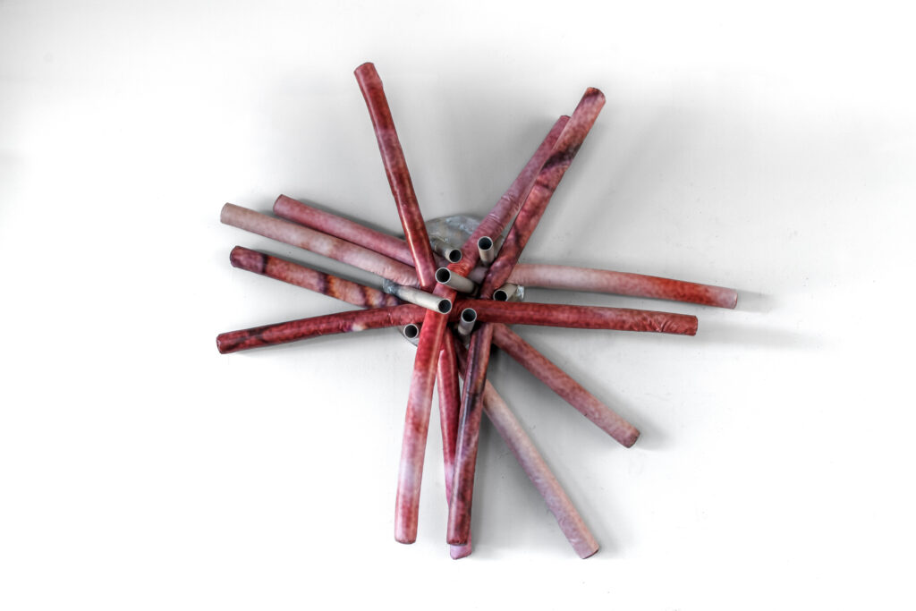 Wall-hanging sculpture in the shape of pool noodles covered with images of human skin printed on vinyl on an aluminum base.
