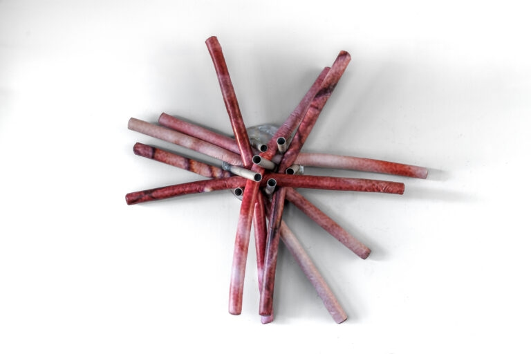 Wall-hanging sculpture in the shape of pool noodles covered with images of human skin printed on vinyl on an aluminum base.